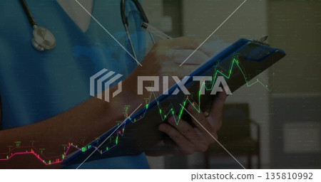 Writing on clipboard clinician wearing scrubs and stethoscope in clinic with digital graph overlay 135810992