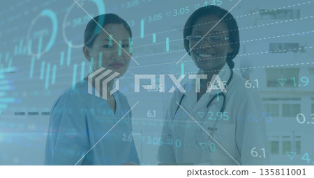 Two female medics standing in clinic viewing data charts, with stethoscope, blue scrubs, lab coat Two female medics standing in clinic viewing data charts, with stethoscope, blue scrubs, lab coat 135811001