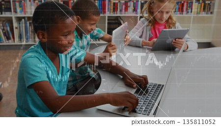 Sitting three students using laptop and tablets at white study table in library, with bookshelves 135811052