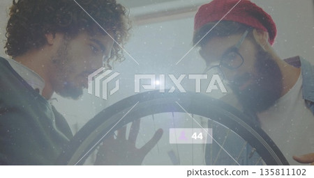 Two men examining spokes on bicycle wheel in repair workshop, with digital overlay showing 44 Two men examining spokes on bicycle wheel in repair workshop, with digital overlay showing 44 135811102