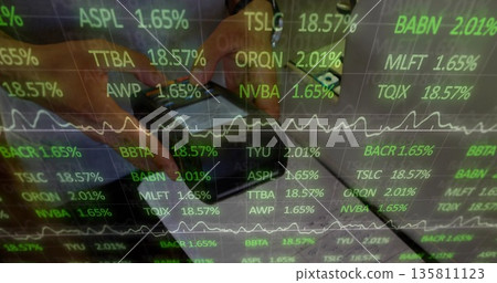 Man holding smartphone and glasses at office desk, with notebook pen and stock ticker overlay 135811123