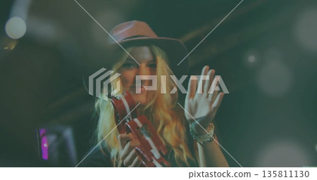 Musician shaking red tambourine and waving under stage lights, with wide-brimmed hat and bracelets Musician shaking red tambourine and waving under stage lights, with wide-brimmed hat and bracelets 135811130
