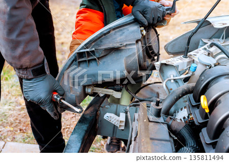 Two maintenance worker on fixing car in driveway during car service while using tools wearing gloves. 135811494