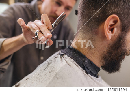 Barber cutting male client hair with scissors and comb. Close up of professional haircut process, precision technique, men grooming service in modern barbershop. Barber cutting male client hair with scissors and comb. Close up of professional haircut process, precision technique, men grooming service in modern barbershop. 135811594