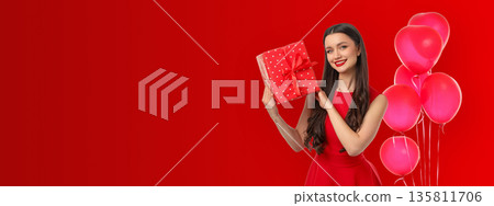 Young woman in a red dress smiles while holding a gift box Young woman in a red dress smiles while holding a gift box 135811706