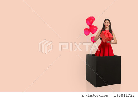 Young woman holds a gift box and stands beside red balloons Young woman holds a gift box and stands beside red balloons 135811722