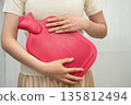 Woman using hot water bottle to relieve menstrual abdominal pain. 135812494