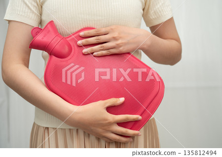Woman using hot water bottle to relieve menstrual abdominal pain. Woman using hot water bottle to relieve menstrual abdominal pain. 135812494
