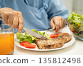 Asian elderly woman patient eating pork chop stake and vegetable salad for healthy food in hospital. 135812498