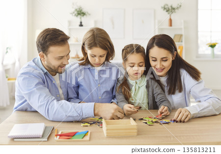 Smiling family playing educational board game, collecting colorful jigsaw puzzles together at home. 135813211