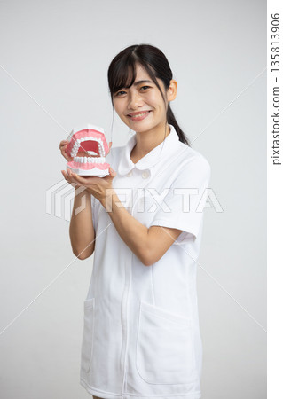 A young woman in a white coat smiling while holding a dental model in front of a white background 135813906