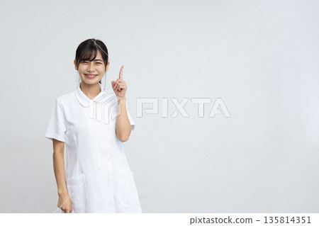 一位身穿白大褂的年輕女子在白色背景前微笑，舉起食指。 135814351