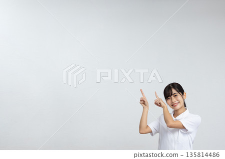 A young woman in a white lab coat smiling and pointing at a large copy space in front of a white background A young woman in a white lab coat smiling and pointing at a large copy space in front of a white background 135814486