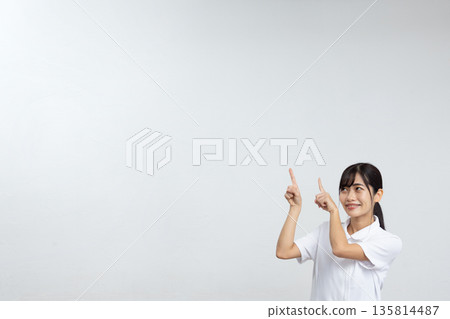 一位身穿白色實驗服的年輕女子麵帶微笑，指著白色背景前的一大片空白區域。 135814487