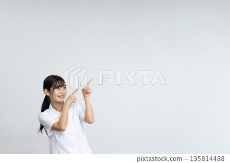 A young woman in a white lab coat smiling and pointing at a large copy space in front of a white background A young woman in a white lab coat smiling and pointing at a large copy space in front of a white background 135814488