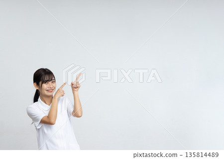 A young woman in a white lab coat smiling and pointing at a large copy space in front of a white background A young woman in a white lab coat smiling and pointing at a large copy space in front of a white background 135814489