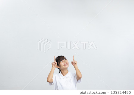 A young woman in a white lab coat smiling and pointing at a large copy space in front of a white background 135814490