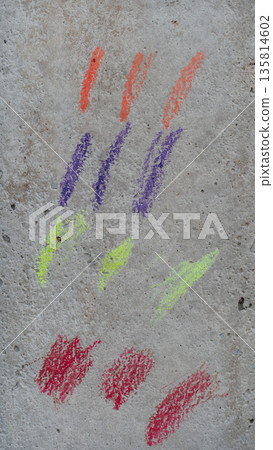Simple yet vibrant display of colorful crayon or chalk swatches on a rough textured grey surface likely concrete. Strokes are divided into four distinct color groups orange purple lime green and red. 135814602