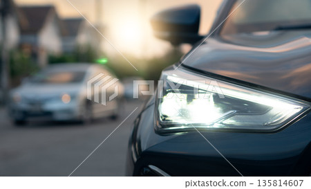 Detail Shot of modern car front LED headlight. Luxury automobile exterior part with reflection. Transportation and vehicle technology on the road inside the village. 135814607