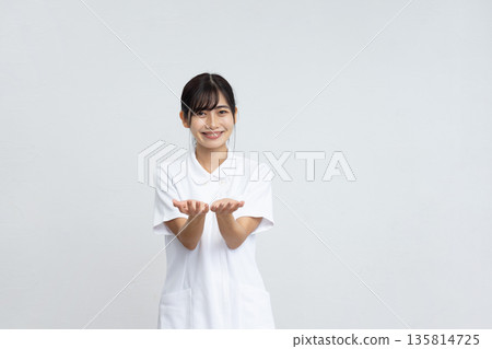 A young woman in a white coat smiling and holding her hands in front of a white background 135814725
