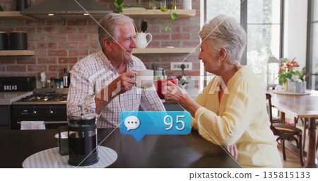 Chatting senior couple in plaid shirt and sweater holding coffee mugs at island with French press Chatting senior couple in plaid shirt and sweater holding coffee mugs at island with French press 135815133