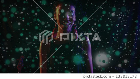Performing artist wearing red tassel earrings standing on stage, under green and white light spots Performing artist wearing red tassel earrings standing on stage, under green and white light spots 135815178