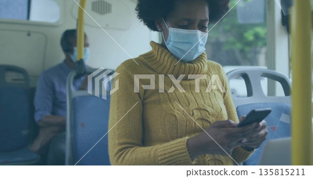 Woman wearing mustard yellow sweater and medical mask holding smartphone on bus, with handrails 135815211