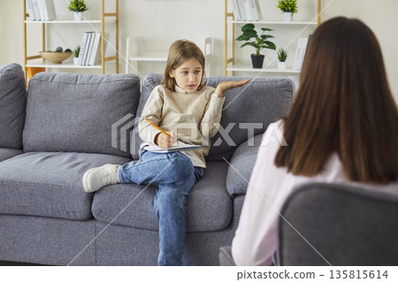 Kid discussing feelings with therapist during counseling session on couch 135815614