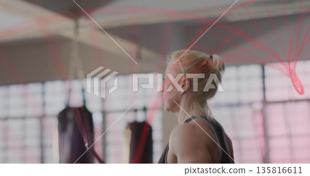 Pulling blonde woman wearing sportswear inside gym with red cable and punching bags, copy space Pulling blonde woman wearing sportswear inside gym with red cable and punching bags, copy space 135816611