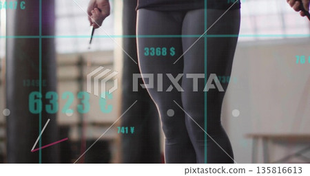 Jumping woman in athletic wear at gym studio, with punching bag, jump rope, teal currency grid Jumping woman in athletic wear at gym studio, with punching bag, jump rope, teal currency grid 135816613