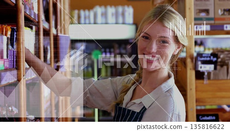 Employee in striped apron arranging packaged goods in aisle, with wooden shelves and digital charts Employee in striped apron arranging packaged goods in aisle, with wooden shelves and digital charts 135816622