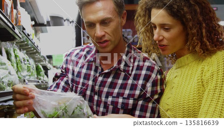 Shoppers in plaid shirt and yellow sweater inspecting sealed salad bag in grocery produce aisle Shoppers in plaid shirt and yellow sweater inspecting sealed salad bag in grocery produce aisle 135816639
