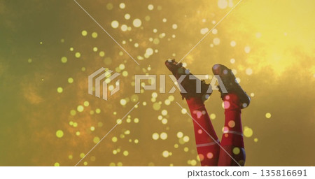 Extending legs wearing red athletic socks and black soccer cleats on golden backdrop, light spots 135816691