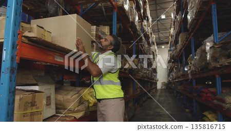Reaching up warehouse worker wearing reflective vest in aisle, with boxes on racks, copy space Reaching up warehouse worker wearing reflective vest in aisle, with boxes on racks, copy space 135816715