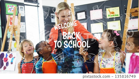 Guiding female art teacher directing children painting on easels in art room, with colorful aprons Guiding female art teacher directing children painting on easels in art room, with colorful aprons 135816749