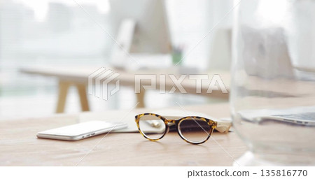 Resting tortoiseshell reading glasses by smartphone on office desk with blurred monitor pitcher Resting tortoiseshell reading glasses by smartphone on office desk with blurred monitor pitcher 135816770