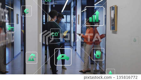 Colleagues discussing data while wearing orange top holding tablet in corridor, floating icons Colleagues discussing data while wearing orange top holding tablet in corridor, floating icons 135816772