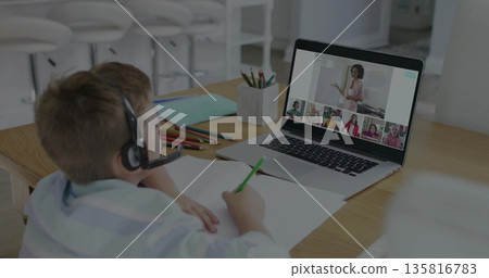 Joining schoolboy wearing headset in online class at home desk, with laptop, pencils, copy space 135816783
