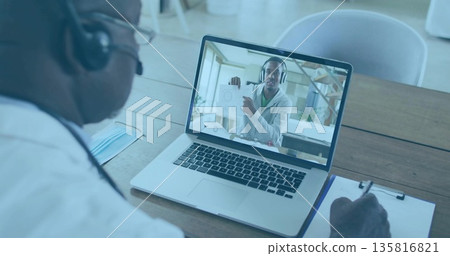 Conducting call doctor taking clipboard notes viewing diagram on laptop in office, with headset Conducting call doctor taking clipboard notes viewing diagram on laptop in office, with headset 135816821
