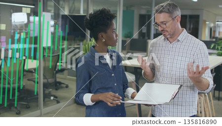 Standing colleagues discussing clipboard data at open-plan office table, with digital bar overlay Standing colleagues discussing clipboard data at open-plan office table, with digital bar overlay 135816890