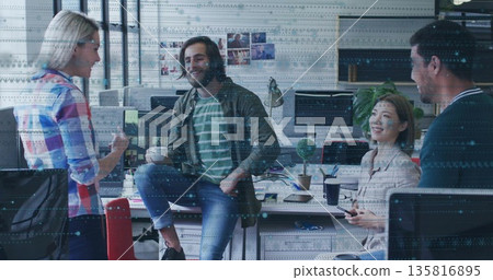 Discussing four colleagues gathering around desks in office, with coffee mugs, monitors, plant 135816895