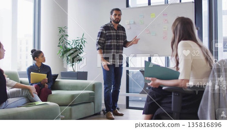 Presenting mid adult man drawing on whiteboard in modern meeting room, with pastel sticky notes 135816896