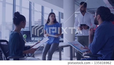 Collaborating office colleagues reviewing printed reports and charts at office desks, with tablet 135816962