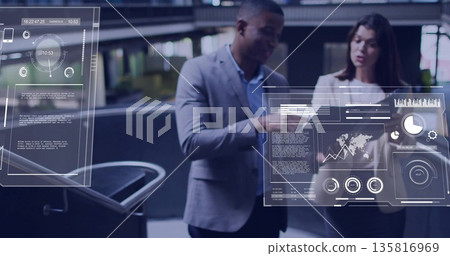 Pointing toward digital dashboards in office atrium, two colleagues in suits analyzing data charts Pointing toward digital dashboards in office atrium, two colleagues in suits analyzing data charts 135816969