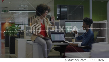 Discussing coworkers in casual wear holding tablet and documents in open plan office, with laptop 135816979