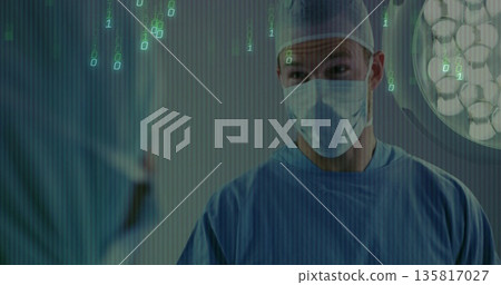 Consulting male surgeon advising colleague in OR under lamp, wearing blue scrubs, masks and caps Consulting male surgeon advising colleague in OR under lamp, wearing blue scrubs, masks and caps 135817027