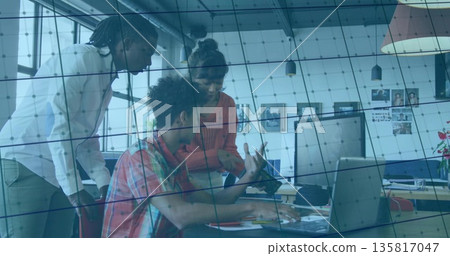 Discussing three professionals collaborating around desk in office, with laptop and smartphone 135817047