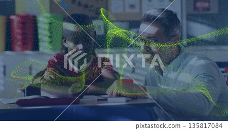 Leaning male educator guiding boy student at school desk, with worksheets and digital overlay 135817084
