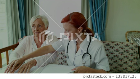 Pointing healthcare worker guiding patient on floral sofa reviewing documents, with stethoscope Pointing healthcare worker guiding patient on floral sofa reviewing documents, with stethoscope 135817123