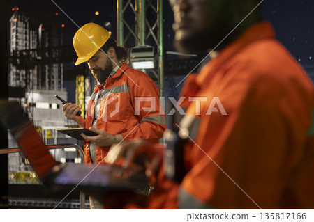 Close up of environmental officer on offshore fossil fuel extraction platform tracking carbon footprint. Drilling rig professional ensuring sustainable practices using notebook during night shift 135817166